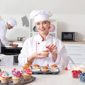 Female confectioner decorating tasty cupcake in kitchen